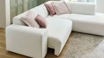 Großzügige Wohnlandschaft in hellen Farben mit roséfarbenen Zierkissen und grün getäfelter Wand – gemütliches, modernes Wohnzimmer mit stilvollem Teppich und Eichenholzboden